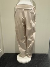 Load image into Gallery viewer, Deck by Decollage tapered sand trousers with a wide waistband, soft pleats, and ankle-length fit. Designed for a sleek, flattering silhouette in a neutral tone-perfect for smart-casual styling.
