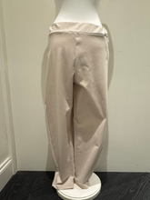 Load image into Gallery viewer, Deck by Decollage tapered sand trousers with a wide waistband, soft pleats, and ankle-length fit. Designed for a sleek, flattering silhouette in a neutral tone-perfect for smart-casual styling.
