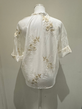 Load image into Gallery viewer, White sheer tie-front blouse with floral embroidery and 3/4 sleeves from Deck by Decollage, styled with dark trousers for a smart casual look.
