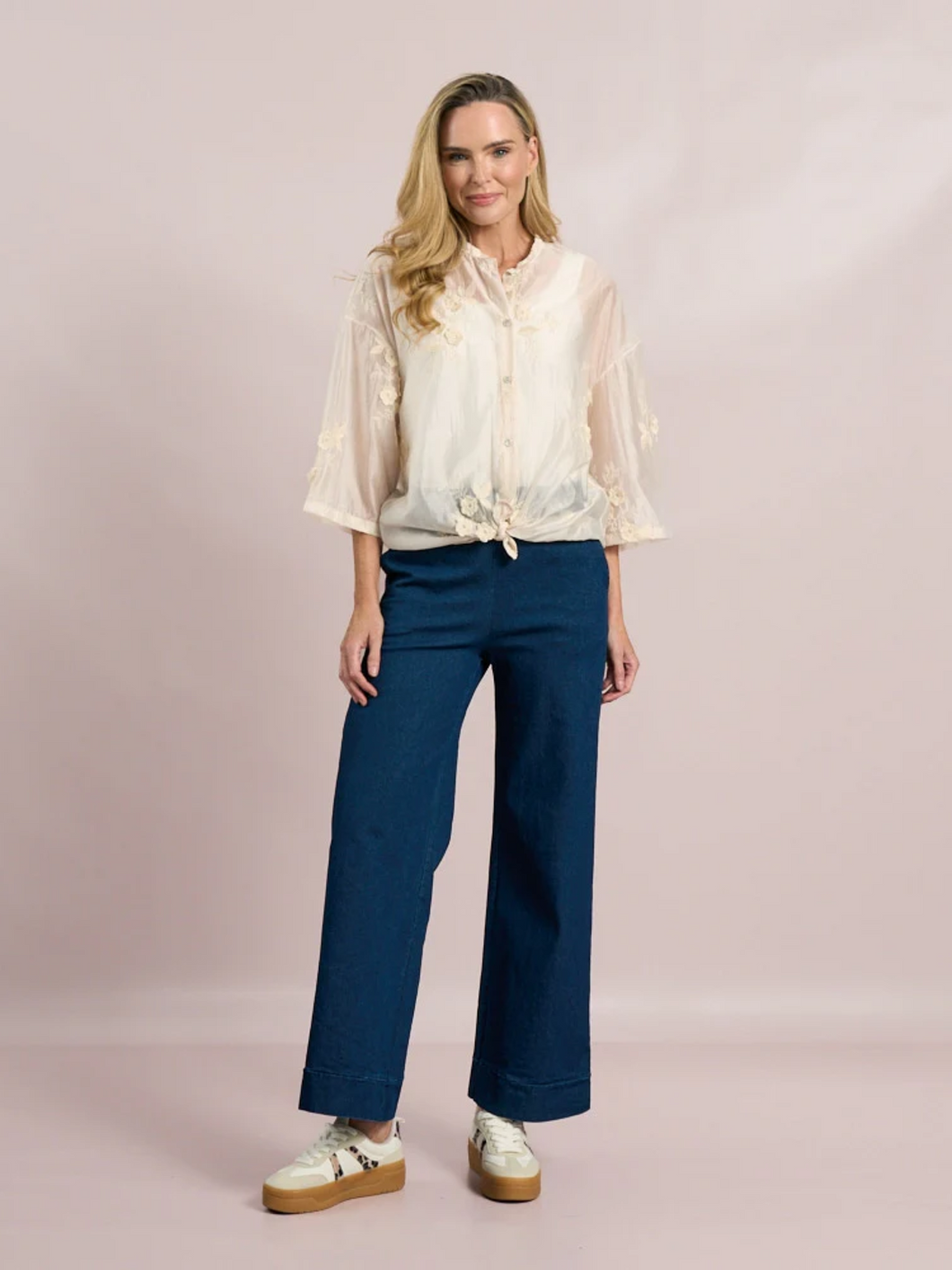 White sheer tie-front blouse with floral embroidery and 3/4 sleeves from Deck by Decollage, styled with dark trousers for a smart casual look.