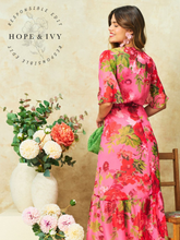 Load image into Gallery viewer, Hope &amp; Ivy Roxanne Floral Dress – sustainable pink floral maxi wrap dress with flutter sleeves and tie waist. Hand-painted red floral design made from 100% recycled materials. Perfect for weddings and summer occasions.
