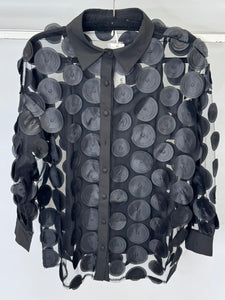 Black sheer blouse with circular patterns on a hanger against a white background