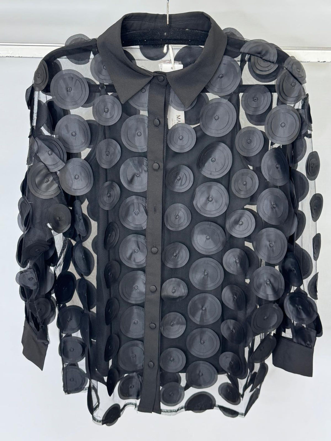 Black sheer blouse with circular patterns on a hanger against a white background
