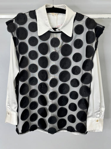 Black polka dot vest over a white shirt on a hanger against a gray background