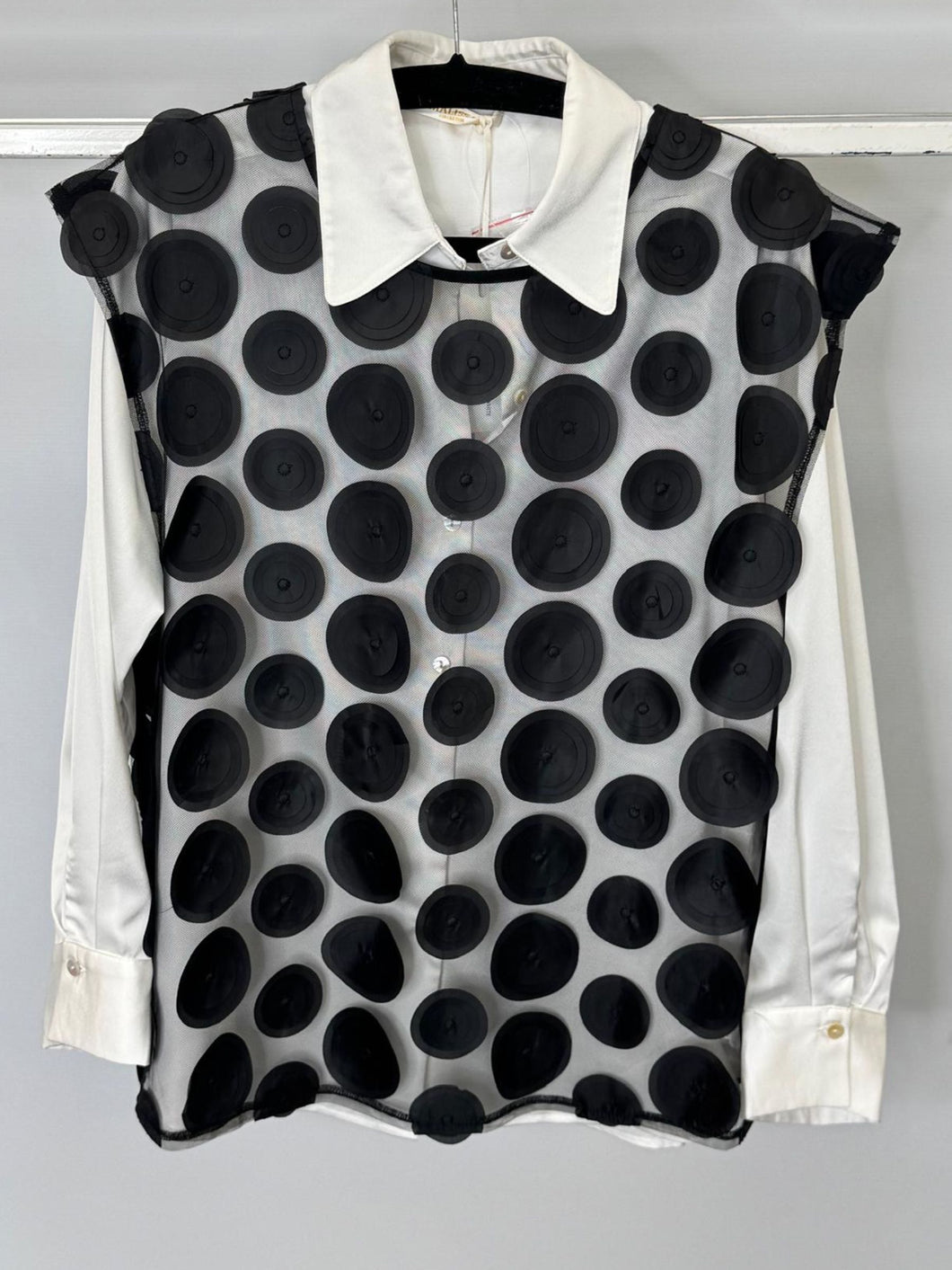 Black polka dot vest over a white shirt on a hanger against a gray background