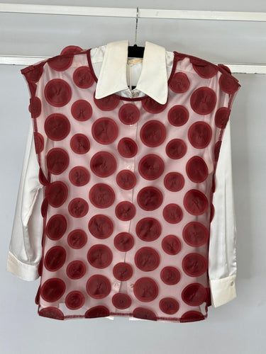 Red polka dot blouse with white collar and sleeves on a hanger against a white background