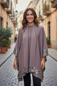 Malissa J WF2496 Stone Poncho and Scarf Set in a soft neutral stone shade, styled with metallic patterned trim, worn by a smiling woman outdoors.