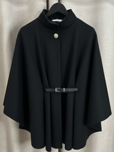 Load image into Gallery viewer, The QBAW25 RR Black Carrie Cape features a structured silhouette with wide sleeves, a high neckline and elegant gold button detailing. Finished with a detachable belt for a flattering fit, this chic cape blends timeless tailoring with modern sophistication - perfect for layering over seasonal outfits.
