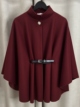 Load image into Gallery viewer, The QBAW25 RR Wine Carrie Cape features a structured silhouette with wide sleeves, a high neckline and elegant gold button detailing. Finished with a detachable belt for a flattering fit, this chic cape blends timeless tailoring with modern sophistication - perfect for layering over seasonal outfits.

